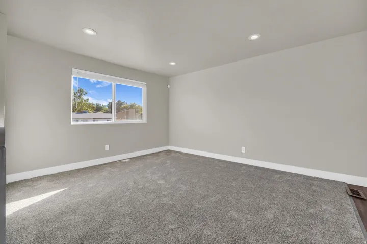 Neutral-toned room featuring a large window, recessed lighting, wall-to-wall carpeting, and white baseboards