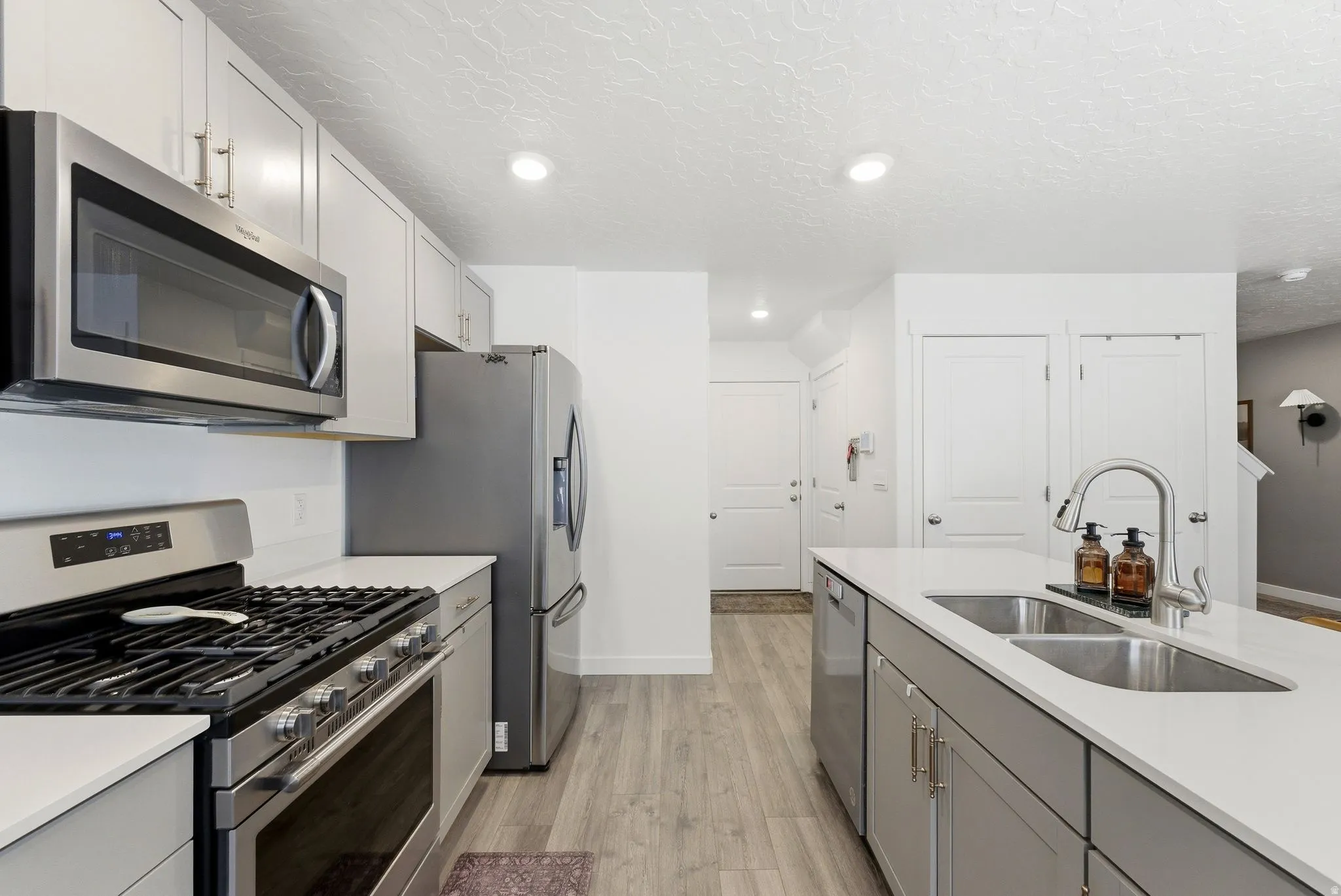 Modern kitchen featuring stainless steel appliances, light gray cabinetry, and a white countertop island with an undermount double-basin sink