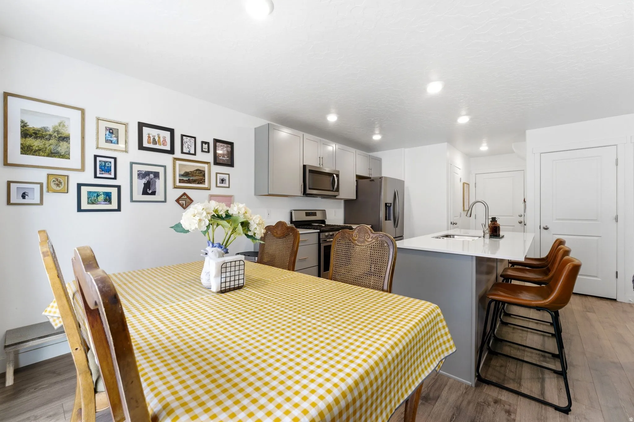 Open-concept kitchen and dining area featuring light gray cabinetry, stainless steel appliances, a center island with countertop seating, and wood-finish flooring