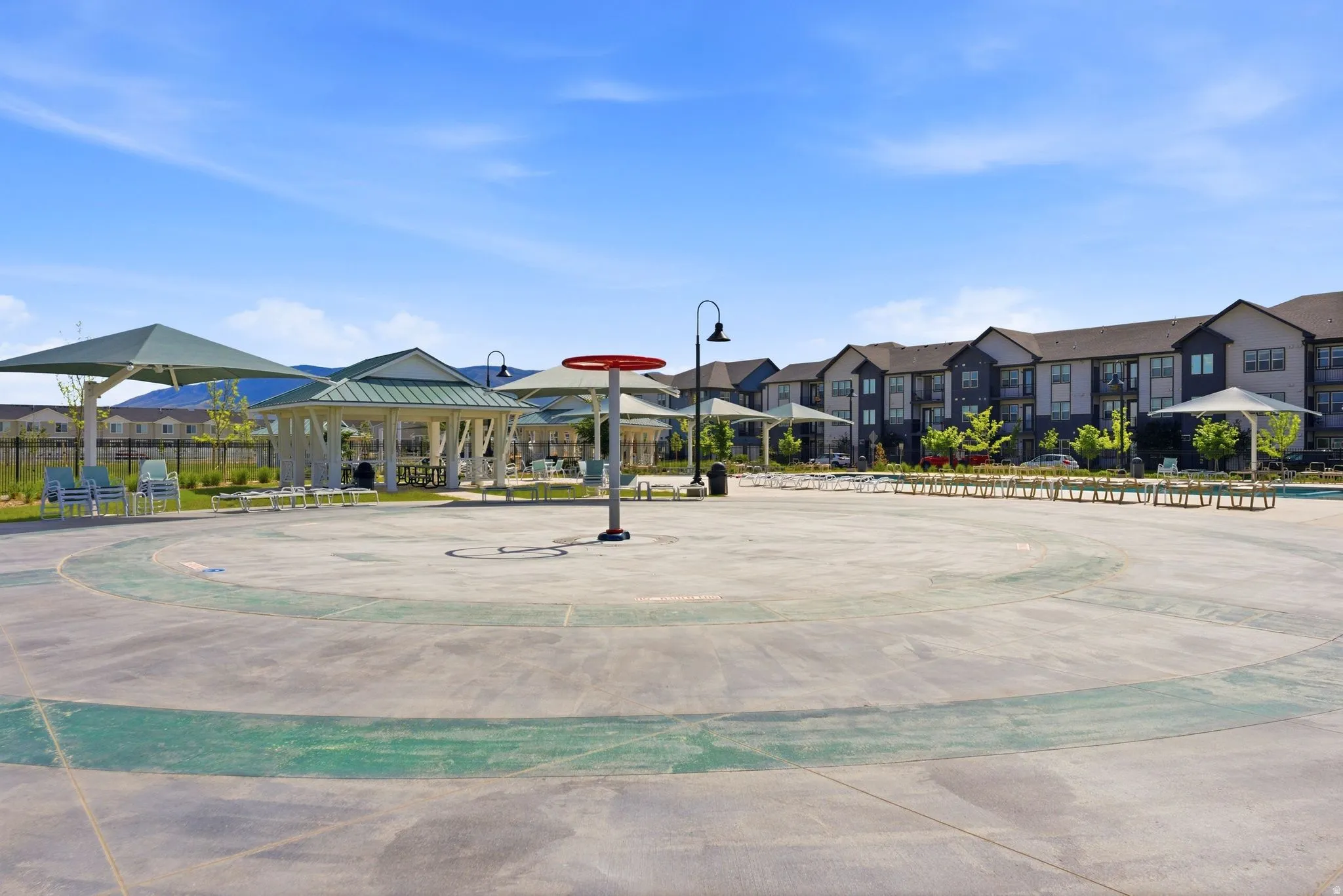 Expansive concrete splash pad with integrated water features, bordered by shaded seating areas