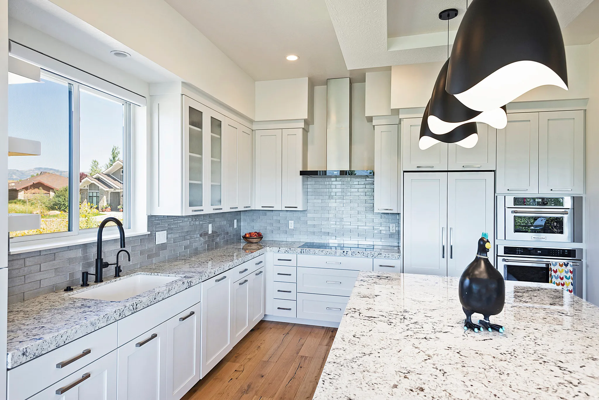 Modern kitchen featuring white cabinetry, light-toned countertops, wood-finish flooring, a contemporary range hood, and integrated stainless steel appliances