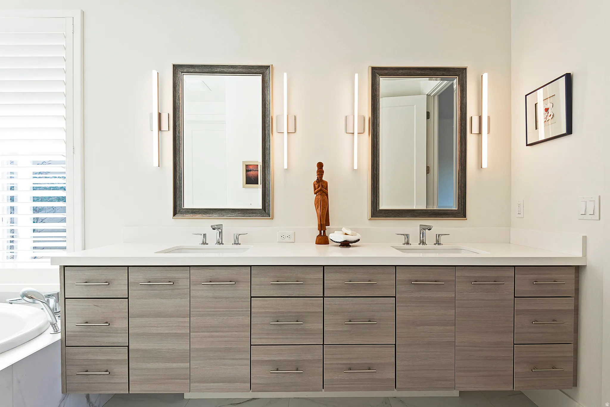 Dual vanity featuring a light wood-finish floating cabinet with extensive drawer storage, two integrated sinks, and a light-toned countertop
