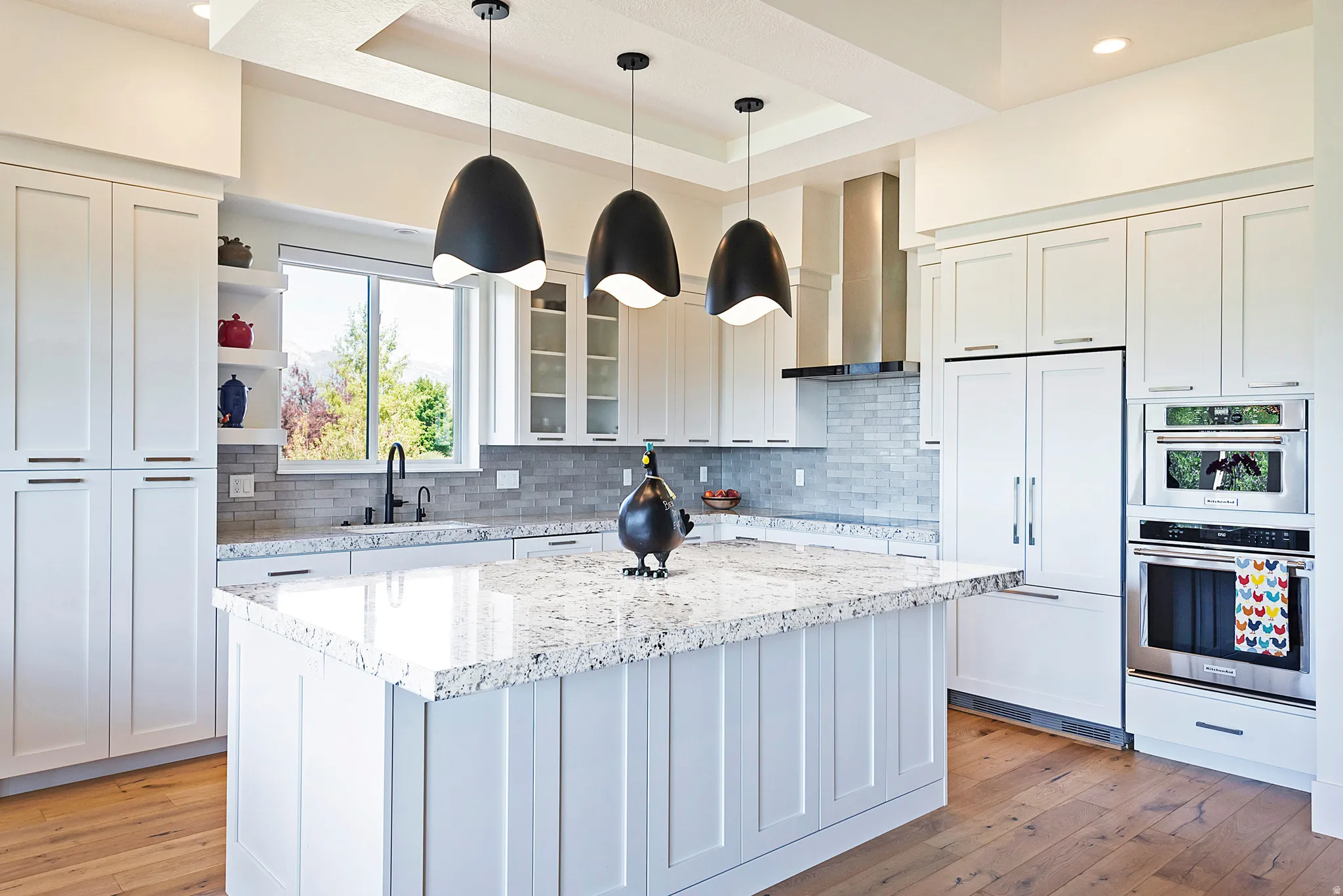 Bright kitchen featuring white cabinetry, a large center island with a speckled countertop, integrated stainless steel appliances, and wood-finish flooring