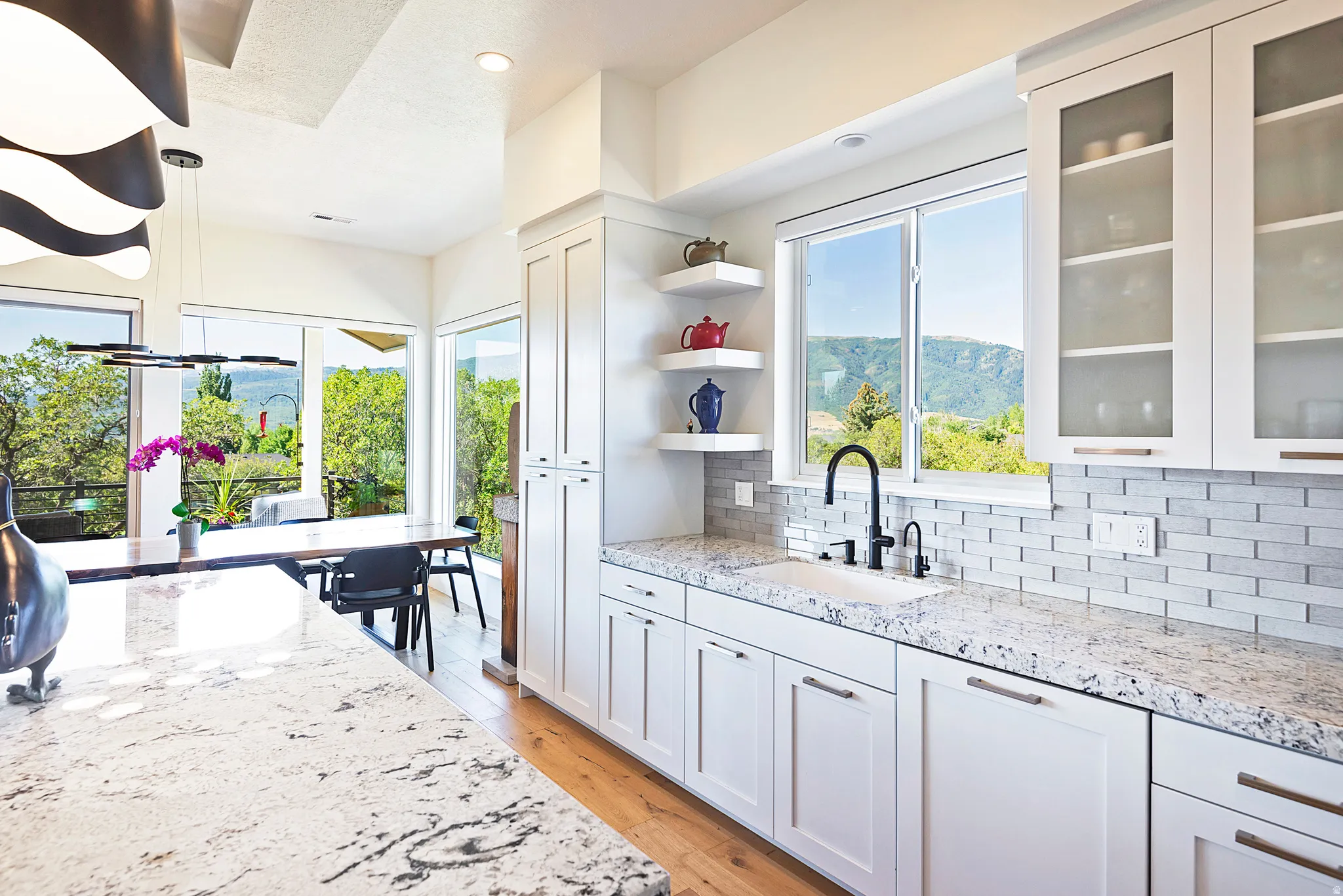 Bright kitchen featuring granite countertops, a subway tile backsplash, white shaker cabinetry, and a black gooseneck faucet