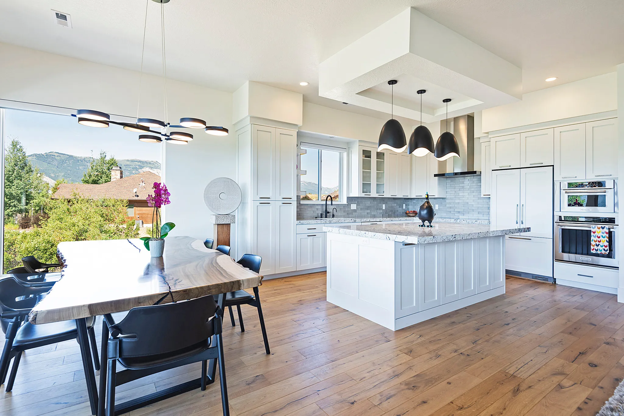 Open-concept kitchen and dining area featuring wide-plank wood-finish flooring, white cabinetry, a central island with a stone countertop, and stainless steel appliances
