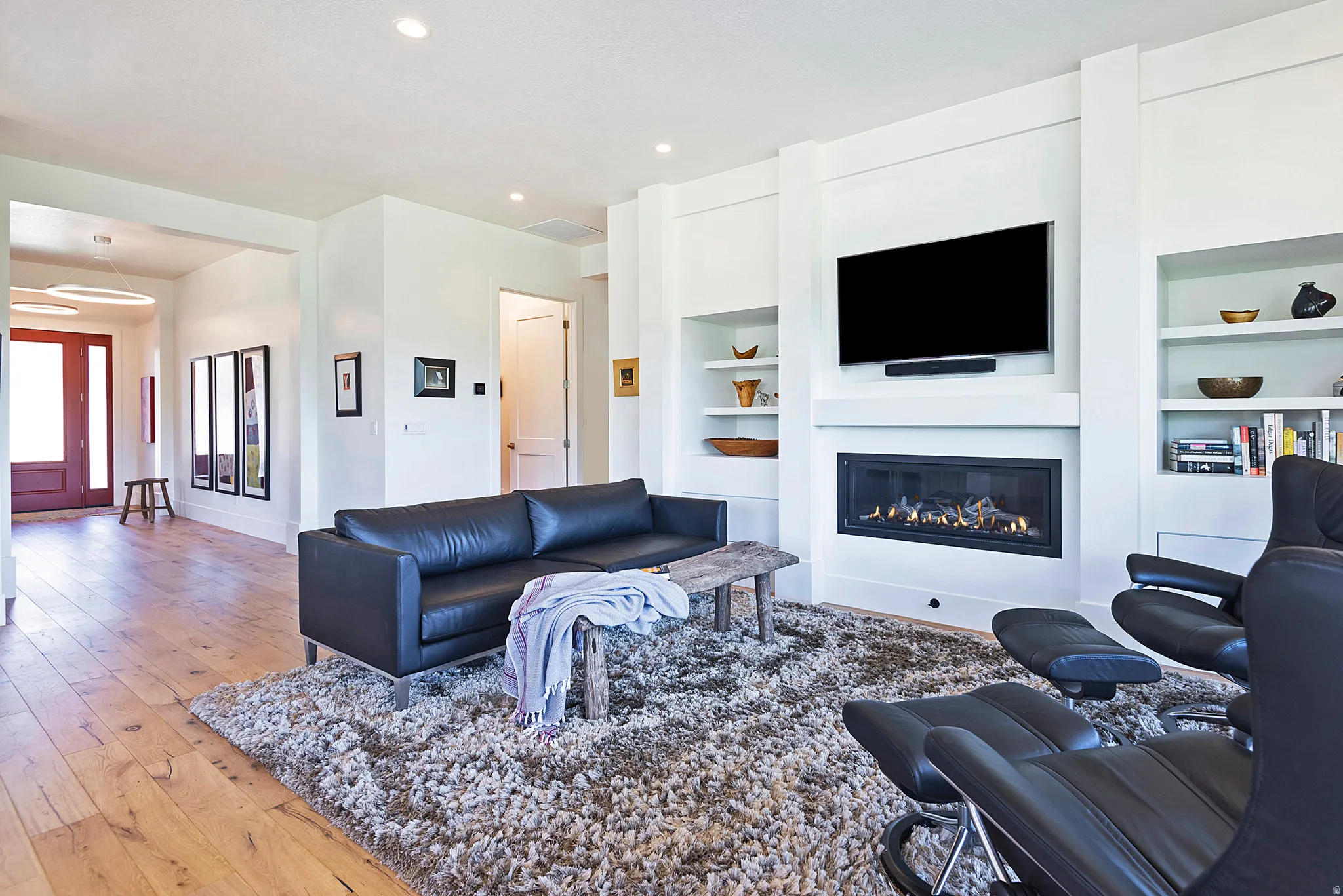 Living room featuring a gas fireplace with integrated television mount, built-in shelving, recessed lighting, and wood-finish flooring