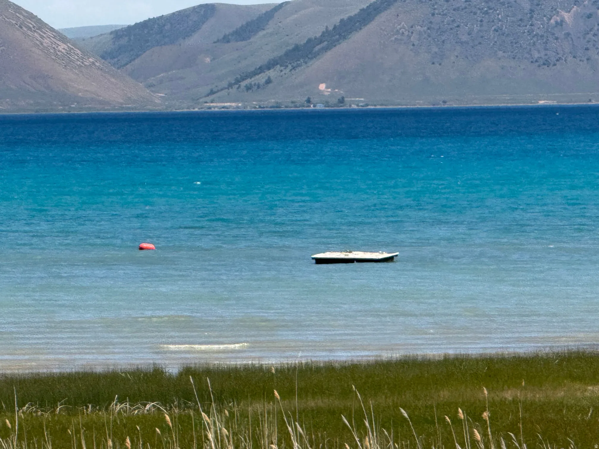 Expansive body of water with varied blue and turquoise hues, bordered by distant mountains