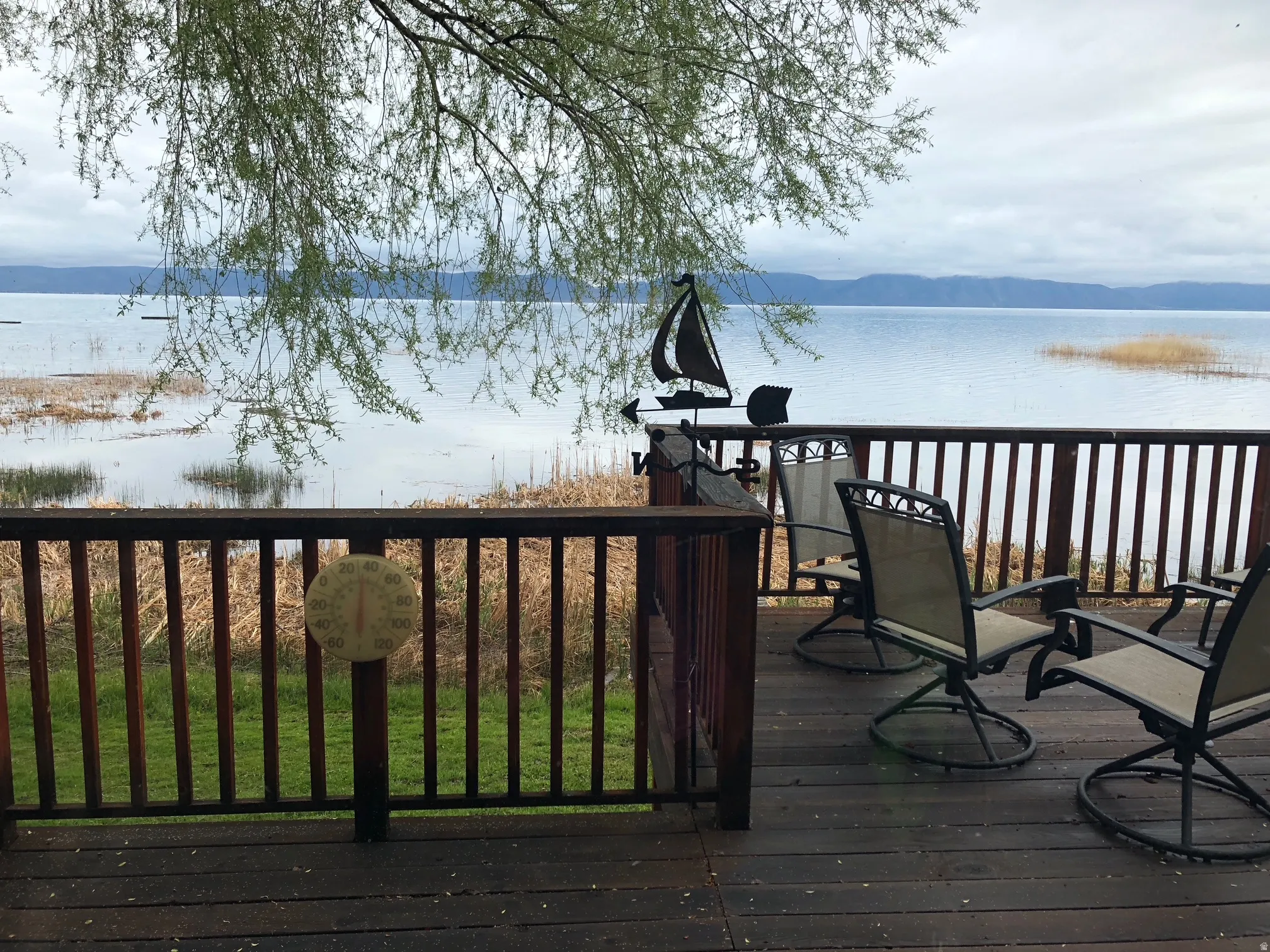 Expansive outdoor deck with dark wood-finish flooring and slatted railing overlooking a body of water with distant mountains