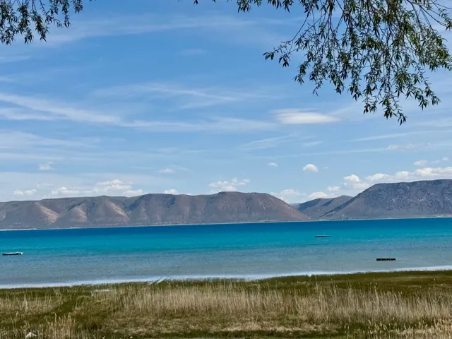 Expansive water frontage with a vibrant turquoise lake, framed by distant mountains and a natural grassy shoreline