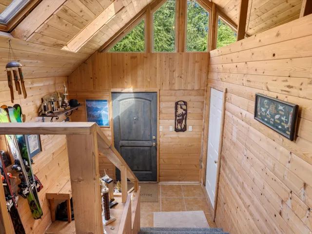 Vaulted ceiling entryway featuring natural wood paneling, an arched transom window, a built-in shelf, and tiled flooring