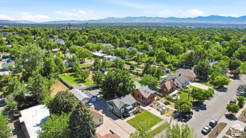 Aerial perspective showcasing a residential neighborhood with abundant mature trees and distant mountain ranges