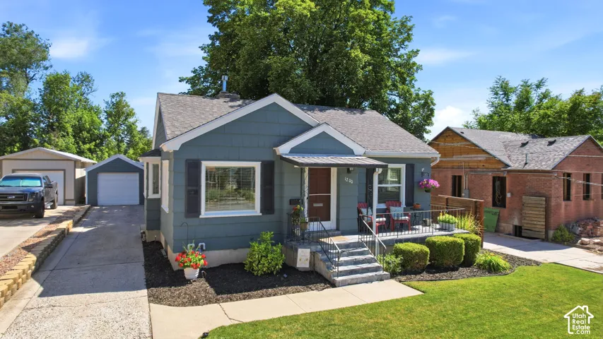 Charming bungalow featuring a covered front porch, concrete steps with wrought iron railing, and a manicured lawn