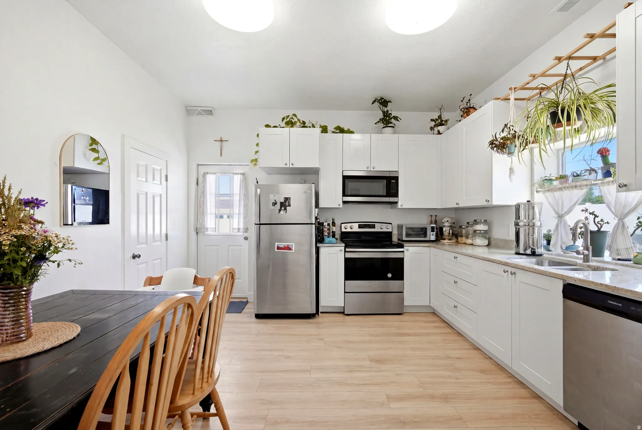 Bright kitchen featuring white cabinetry, light countertops, wood-finish flooring, stainless steel appliances, and a kitchen sink with a window above
