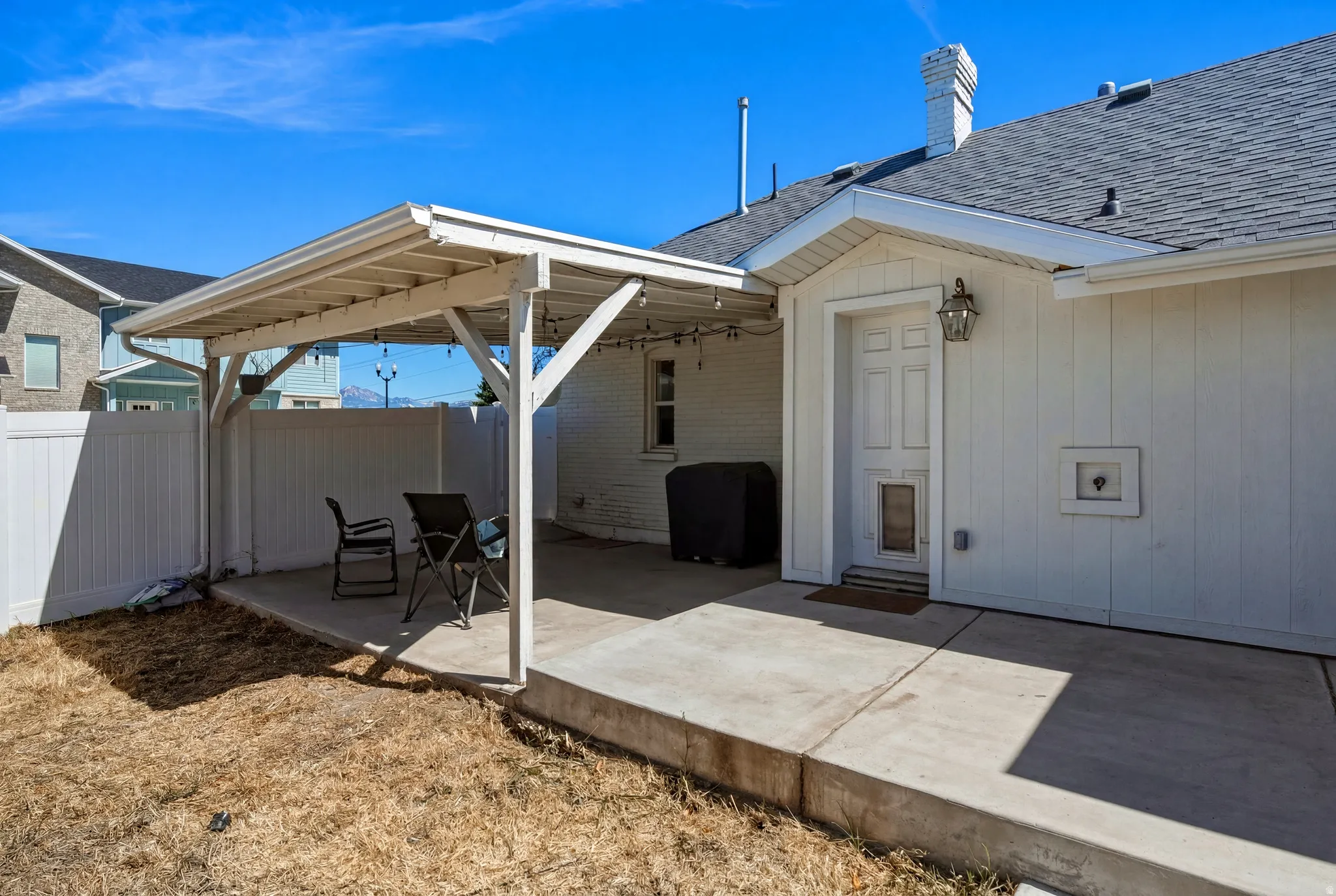 Expansive concrete patio featuring a white pergola, offering an outdoor living area