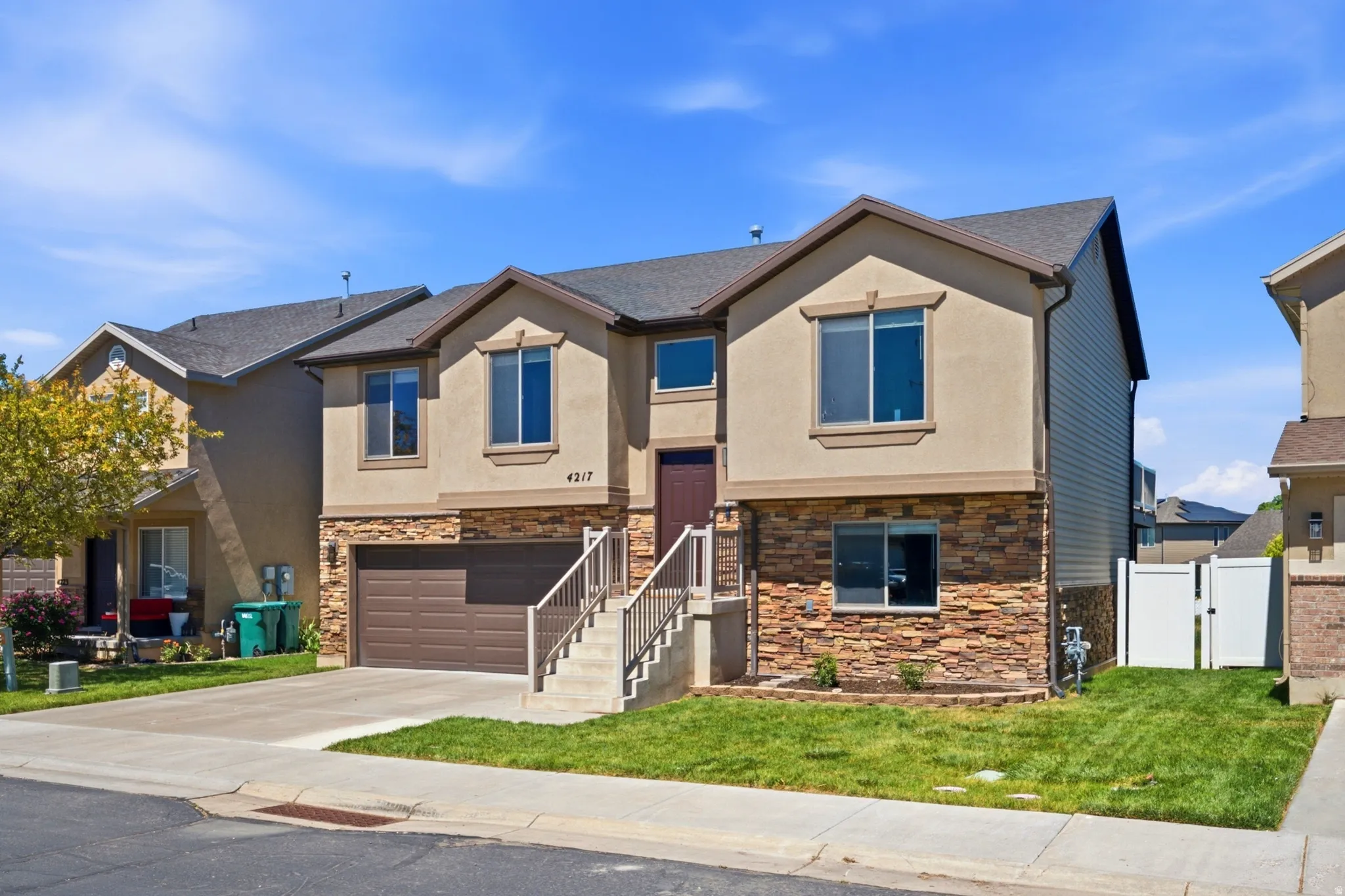 Contemporary stucco and stone-veneer exterior featuring a two-car garage, concrete driveway, and established front landscaping