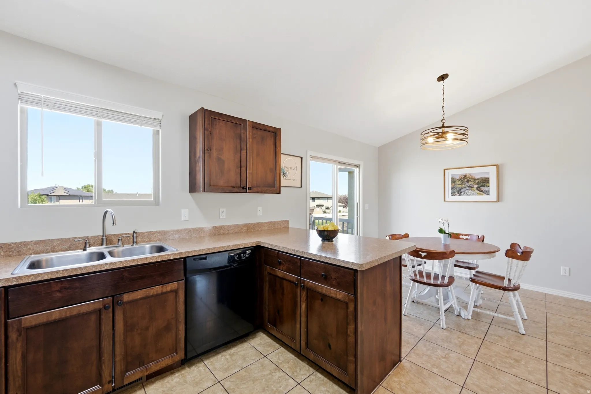 Kitchen featuring dark wood-finish cabinetry, light-toned countertops, a double basin stainless steel sink, black dishwasher, and tile flooring