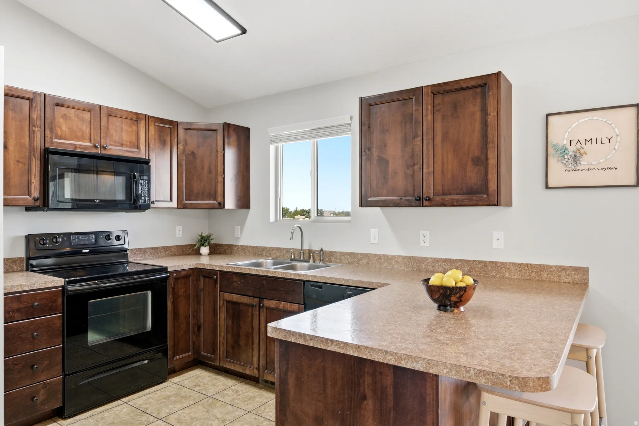 Kitchen featuring wood cabinetry, black appliances, a double basin sink, and a breakfast bar with an integrated countertop