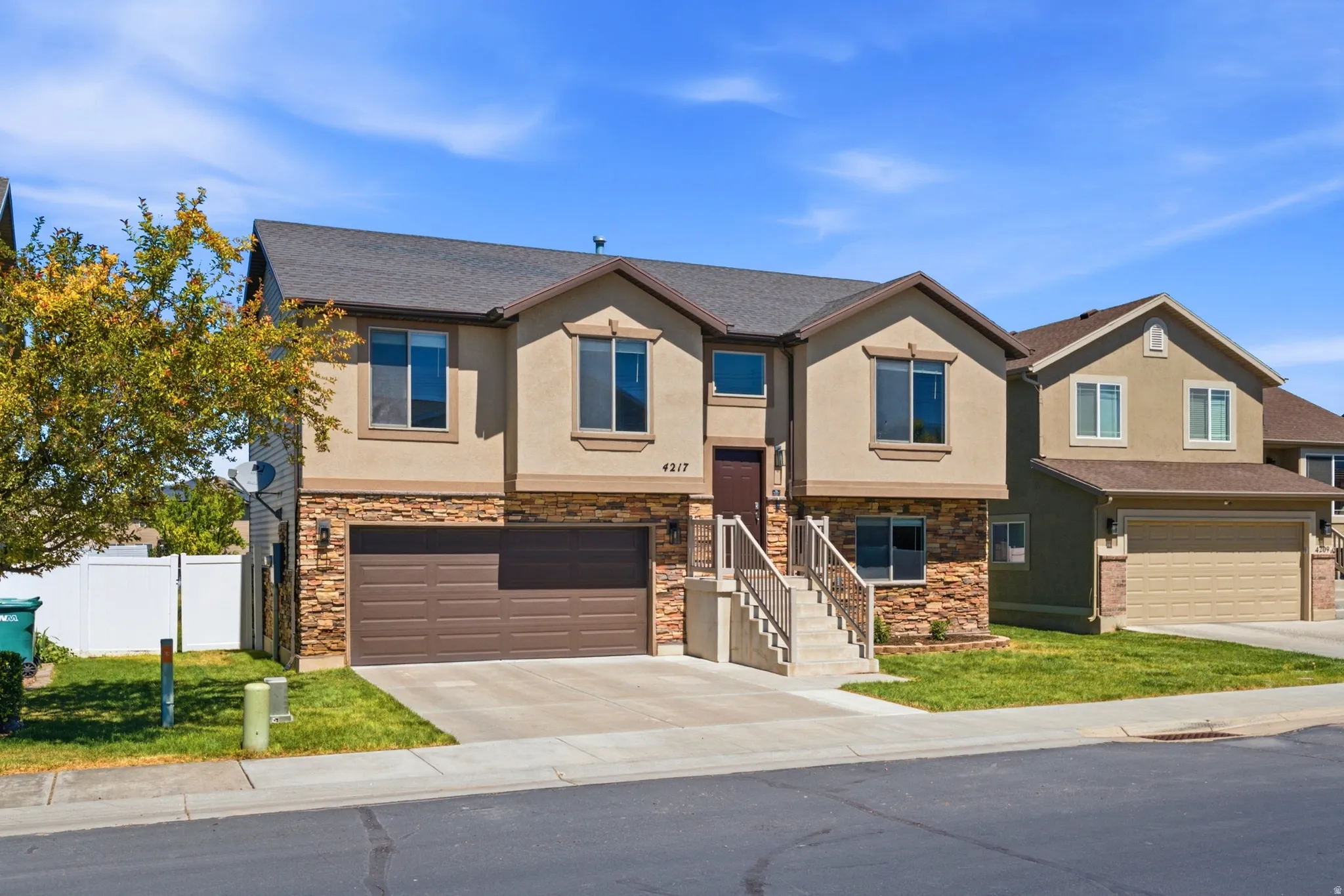 Contemporary stucco and stone-veneer exterior featuring a double-car garage with a brown door, a front entry staircase with metal railings, and a dark brown entry door