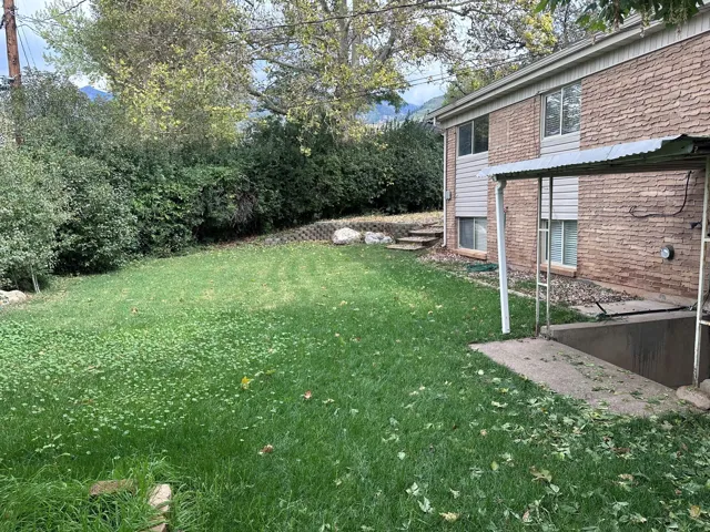 Backyard featuring a green lawn, mature perimeter landscaping, a tiered retaining wall, and exterior brick-finish siding