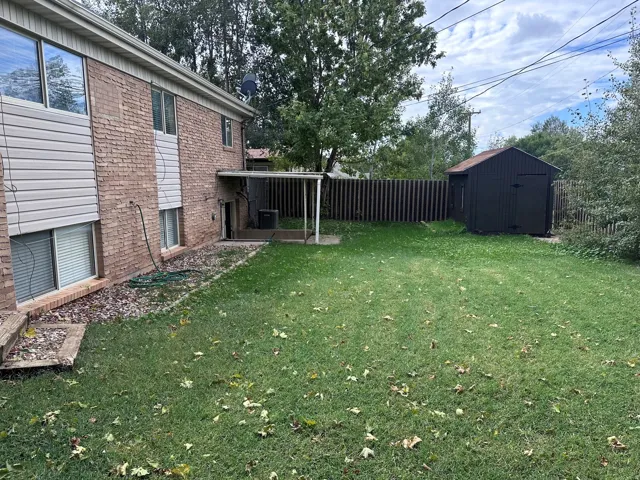 Expansive grass lawn with a storage shed and a covered patio area