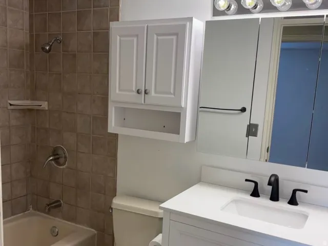 White vanity with black hardware, white rectangular basin, matte black widespread faucet, and large wall mirror with vanity lighting