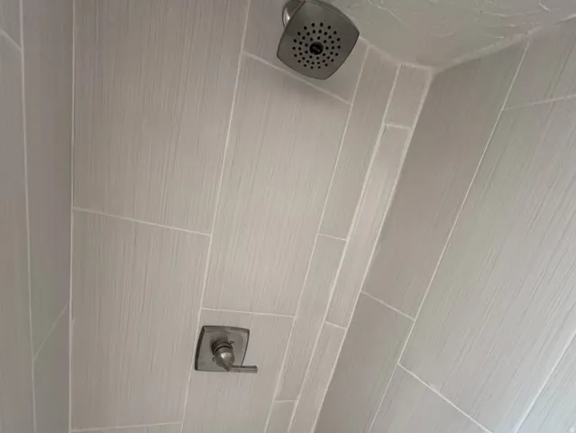 Shower featuring light-toned large format wall tiling, a rainfall showerhead, and a hexagonal mosaic tile floor