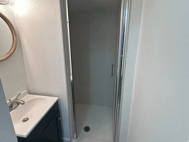 Glass-enclosed shower with subway tile surround, single vanity with integrated sink, dark wood-finish cabinetry, and contemporary wall sconce