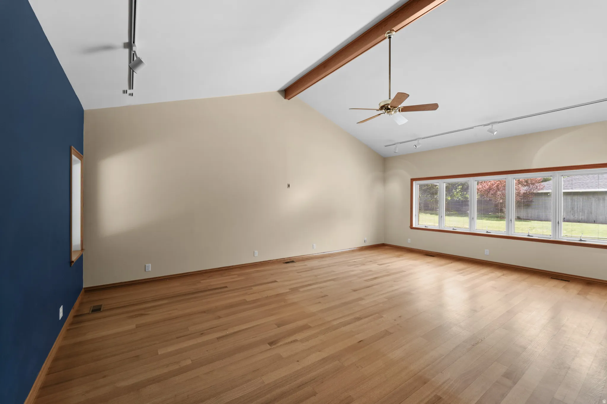Spacious room featuring vaulted ceilings with exposed wood beams, wood-finish flooring, and track lighting