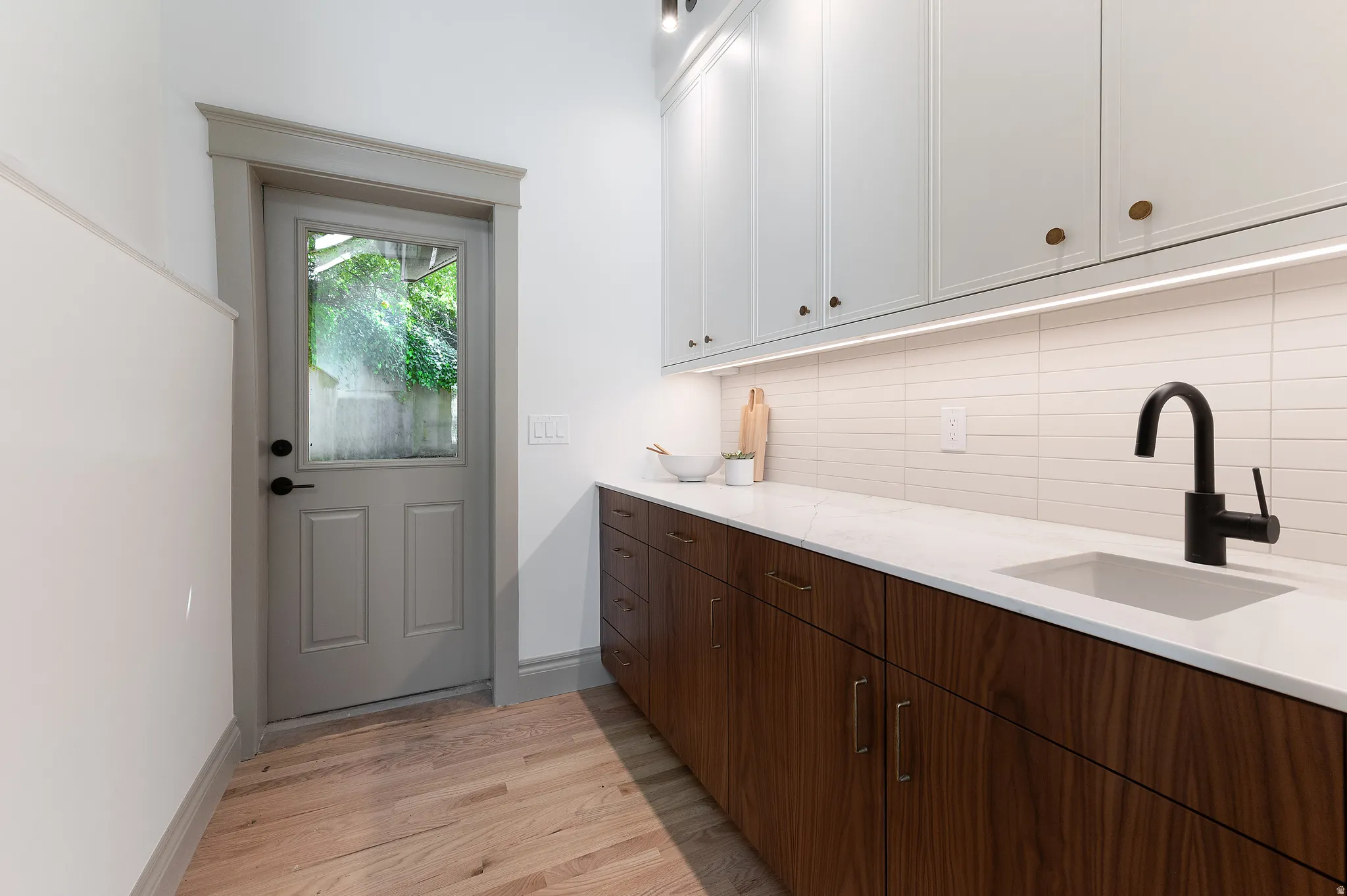 Modern kitchen space featuring a dark wood-finish lower cabinetry, white upper cabinetry, and a white countertop