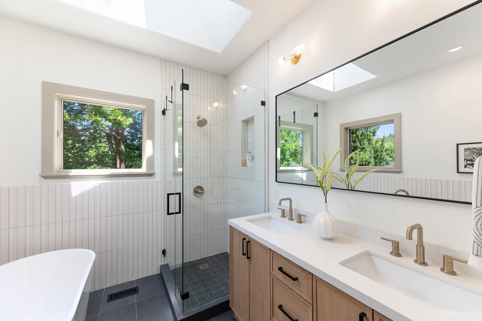 Contemporary bathroom featuring a dual vanity with light wood cabinetry and white countertops
