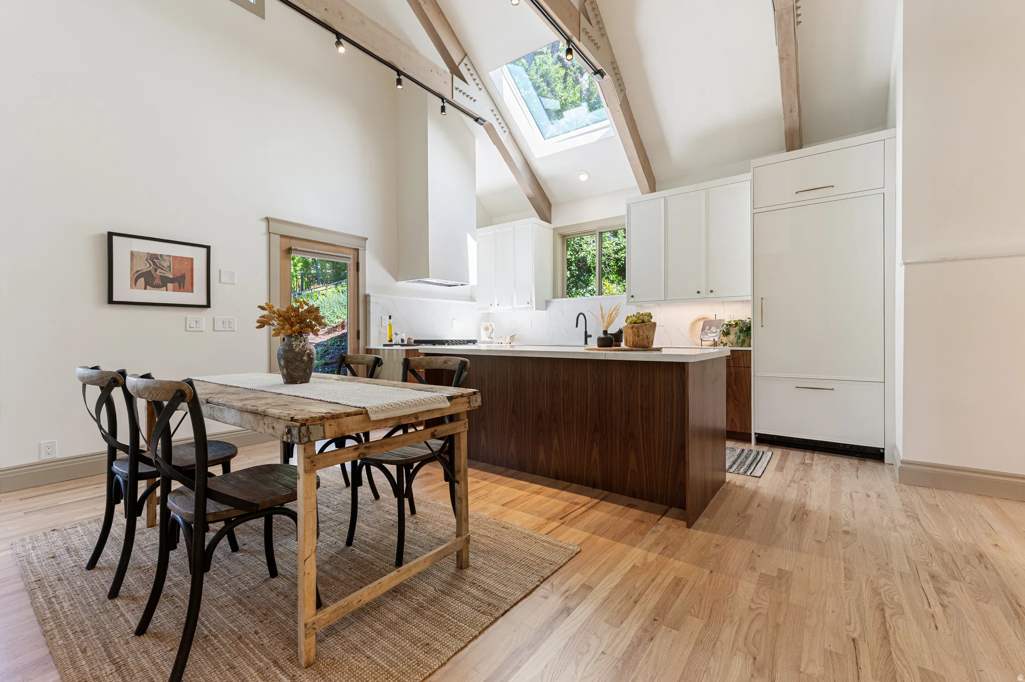 Kitchen and dining space featuring vaulted ceilings, exposed wood beams, skylight, hardwood flooring, and a built-in paneled refrigerator