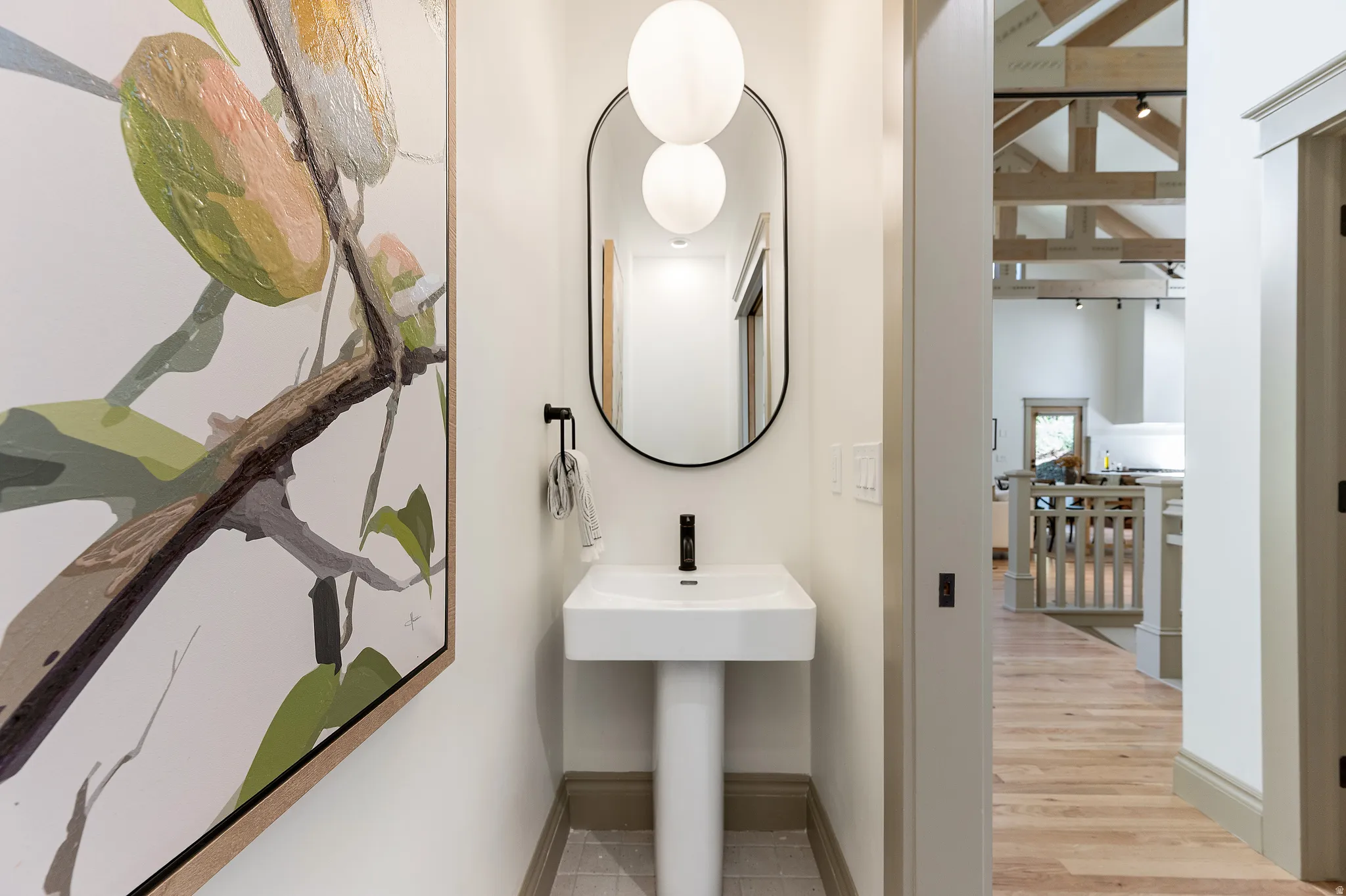 Pedestal sink with a matte black faucet, illuminated by dual globe pendant lights
