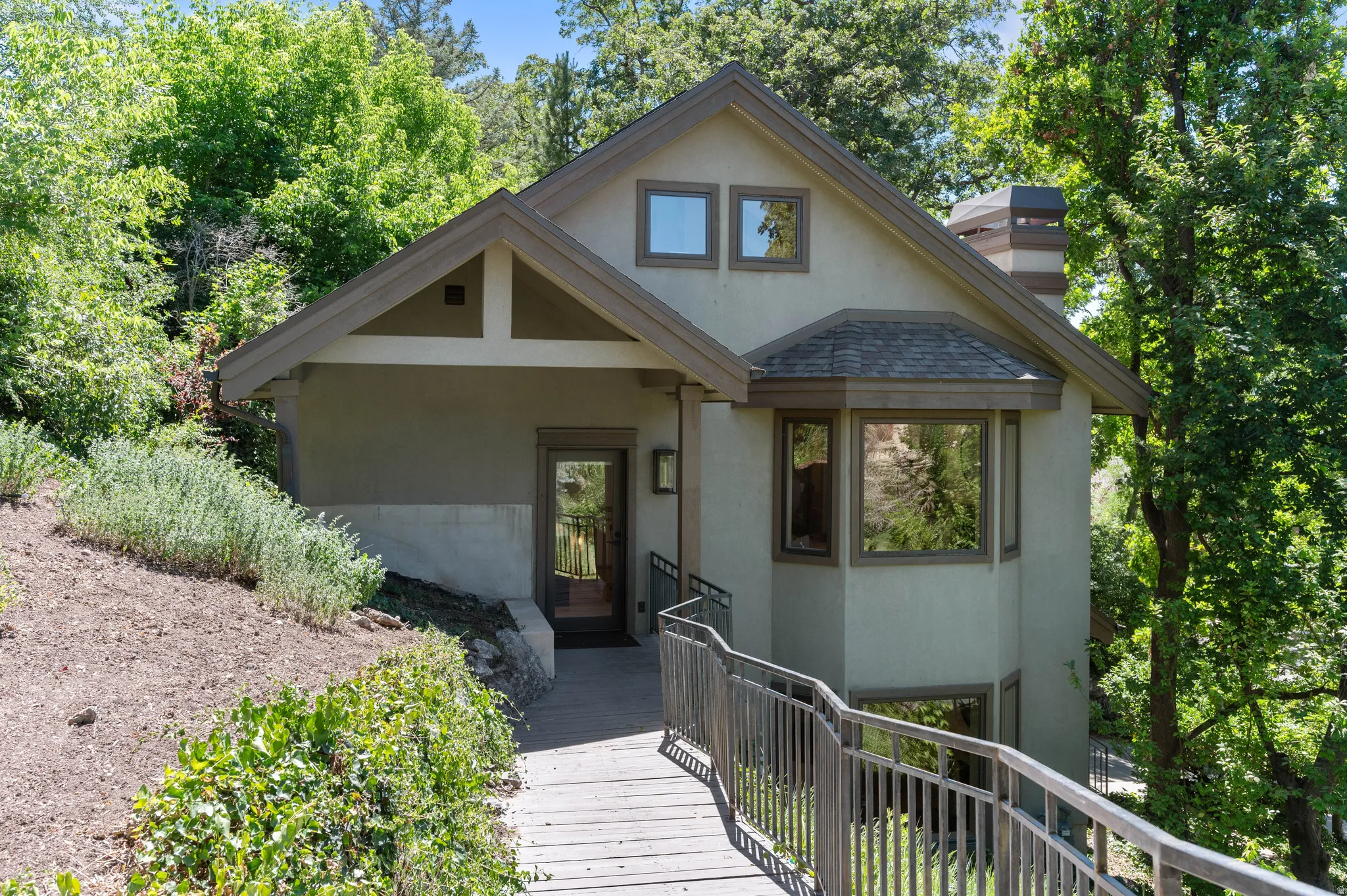 Contemporary exterior featuring stucco siding, multiple gables, a prominent bay window, and an accessible ramp entry with metal railings