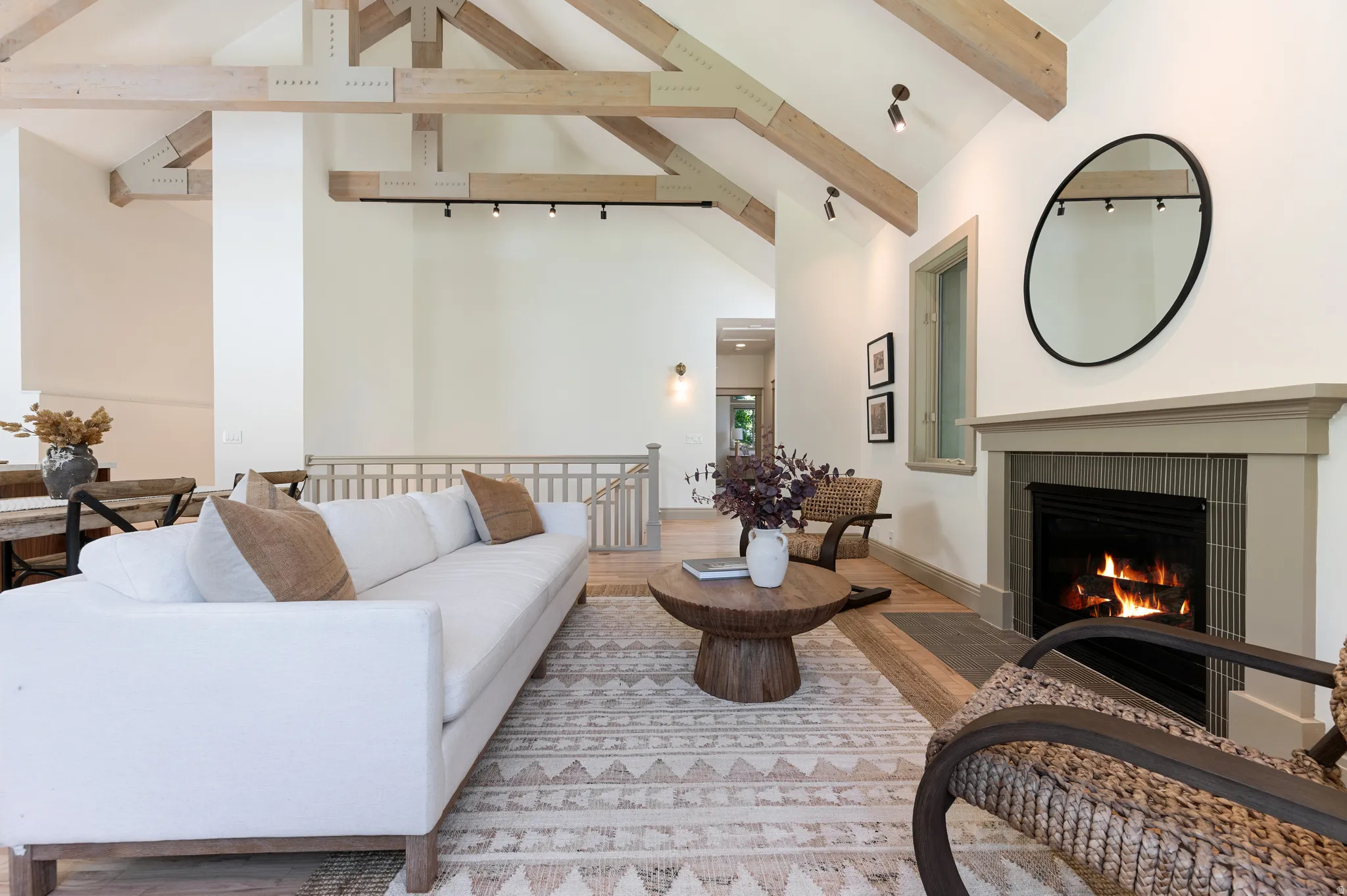 Vaulted ceiling with exposed wood beams, track lighting, and a fireplace featuring a tiled surround and mantel