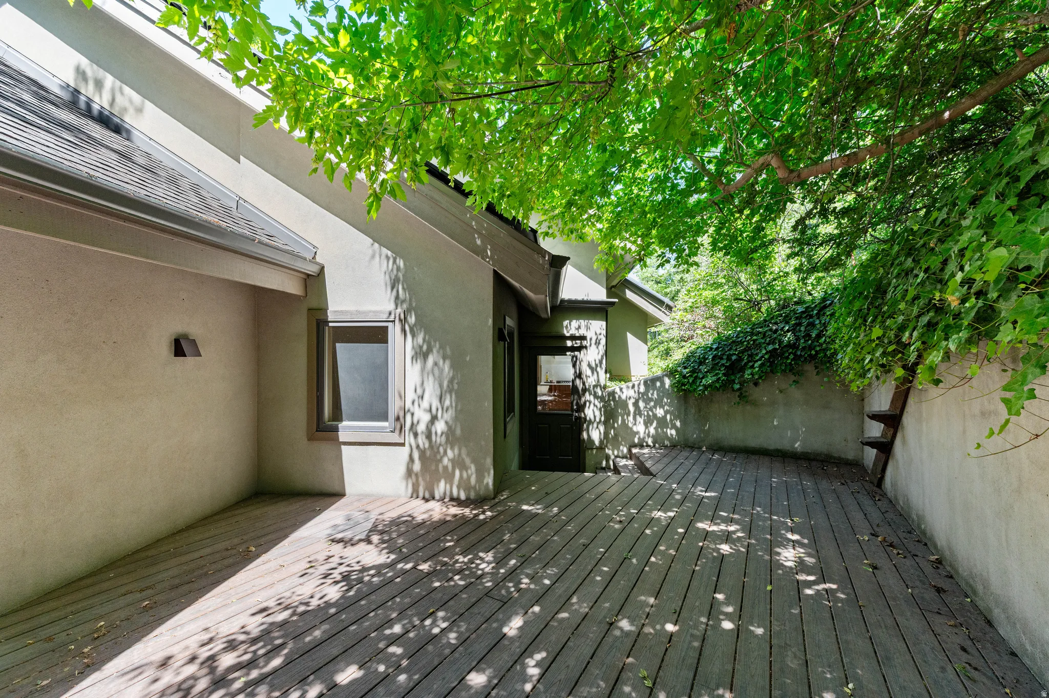 Outdoor wooden deck with a privacy wall and mature overhead foliage