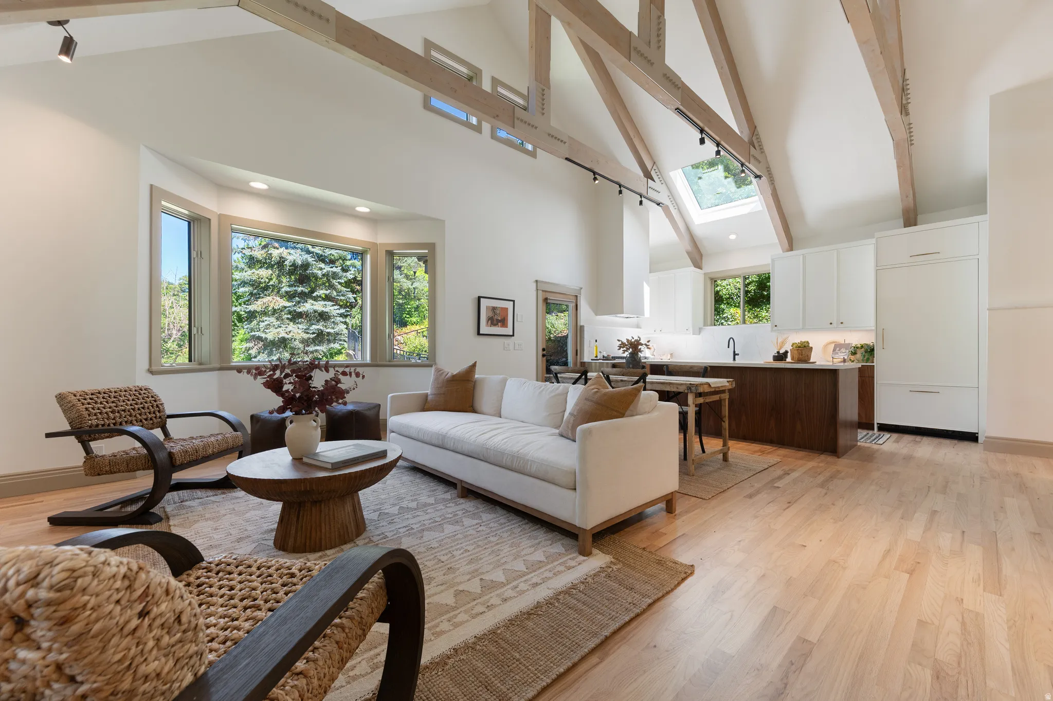 Vaulted ceiling with exposed wood beams, a bay window, and light wood-finish flooring