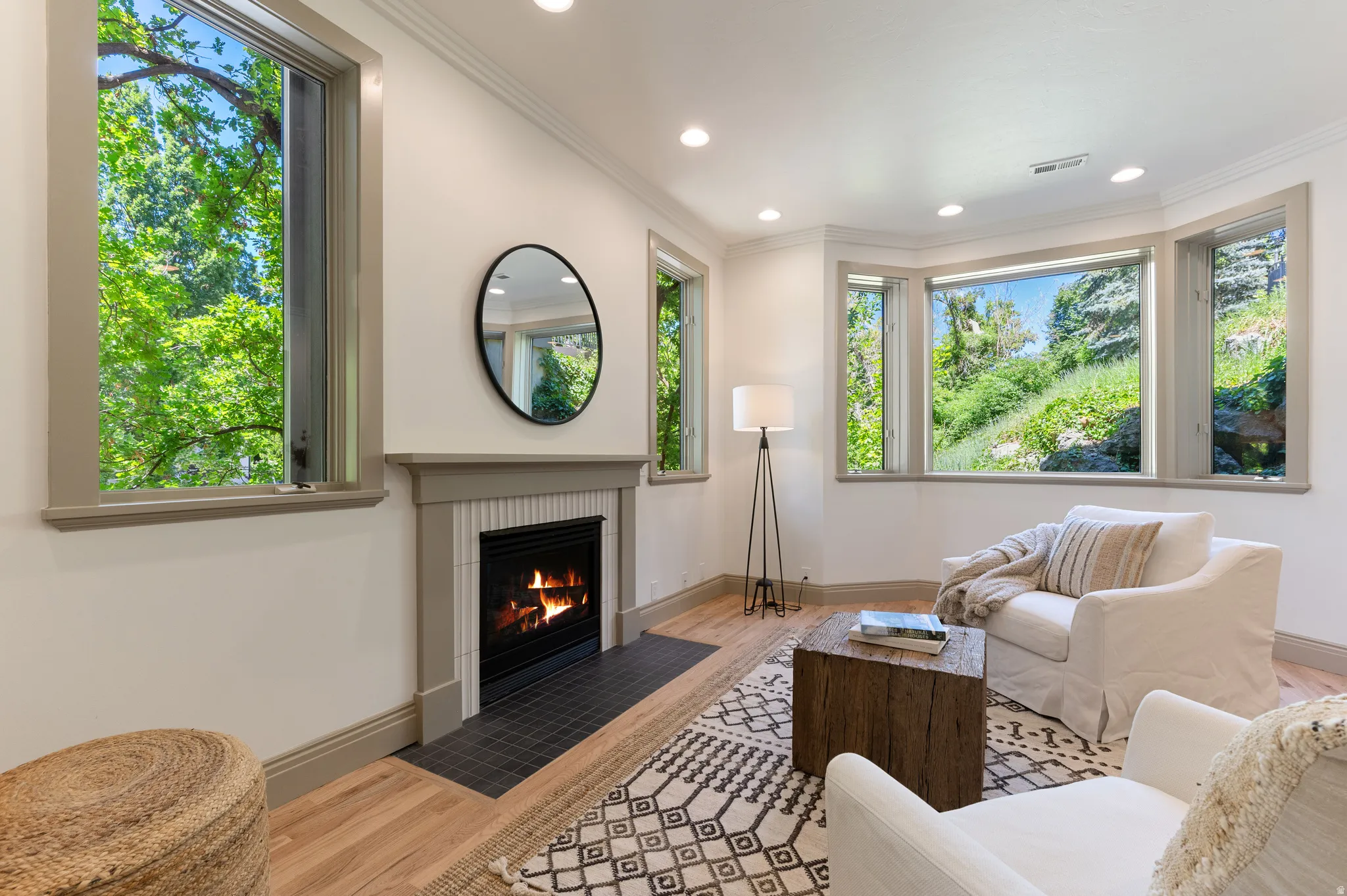 Living area featuring a fireplace with a tiled surround, a bay window with multiple panes, and light wood-finish flooring