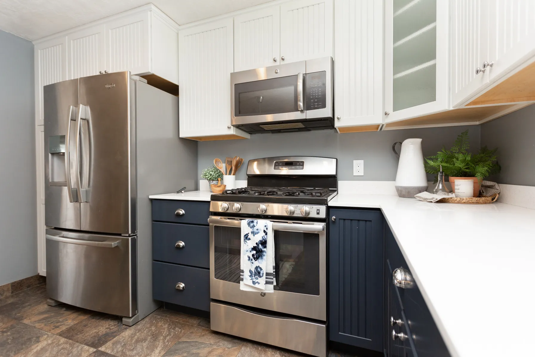 Contemporary kitchen featuring stainless steel appliances, white quartz countertops, two-tone cabinetry with white upper cabinets and navy lower cabinets, and wood-finish flooring