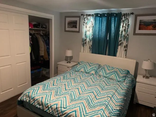 Bedroom featuring wood-finish flooring, light gray walls, a window with curtain rods, and white bi-fold closet doors