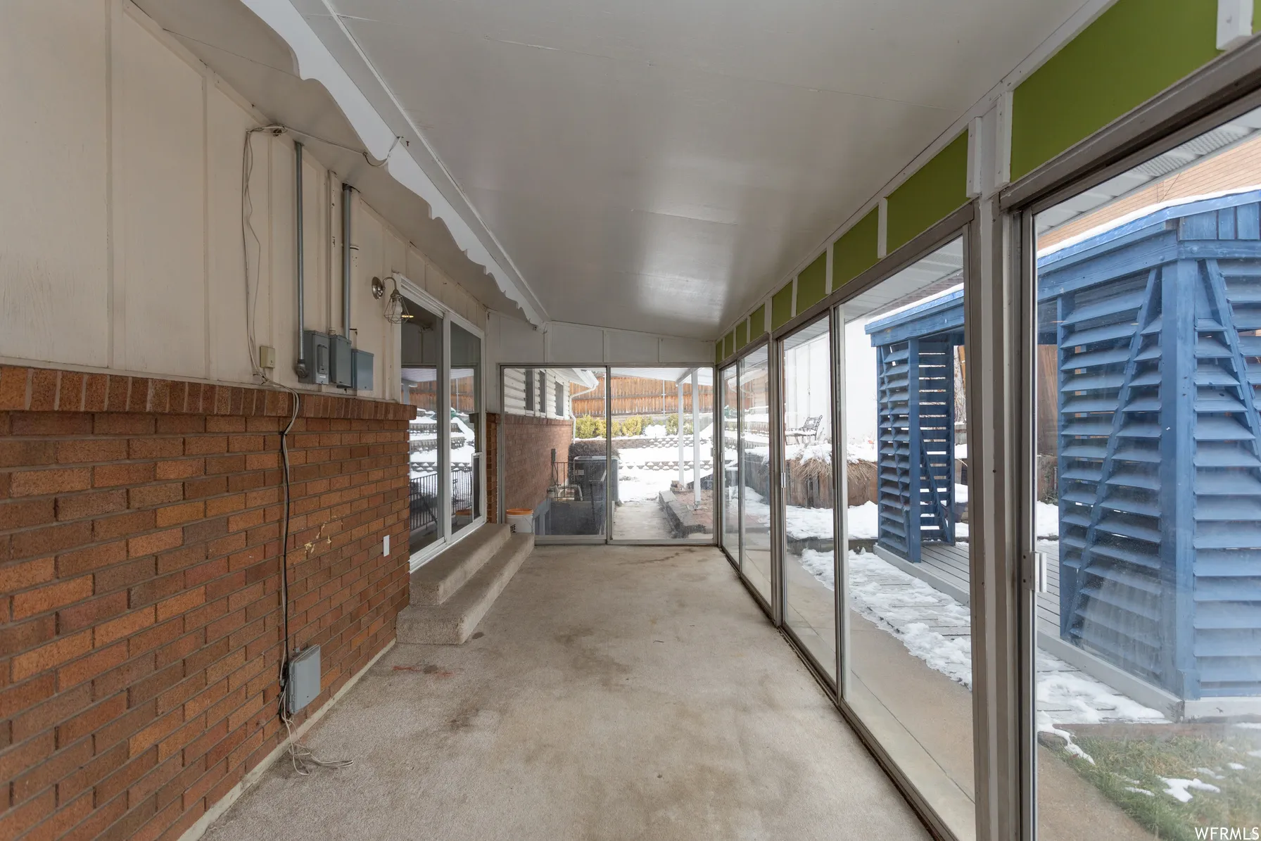 Enclosed patio featuring a concrete floor, red brick knee wall, white vertical siding, and a series of floor-to-ceiling glass panels
