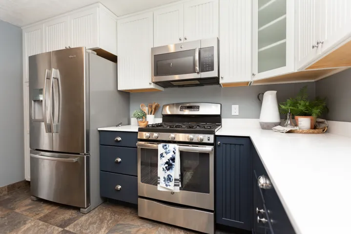 Contemporary kitchen featuring stainless steel appliances, white quartz countertops, two-tone cabinetry with white upper cabinets and navy lower cabinets, and wood-finish flooring