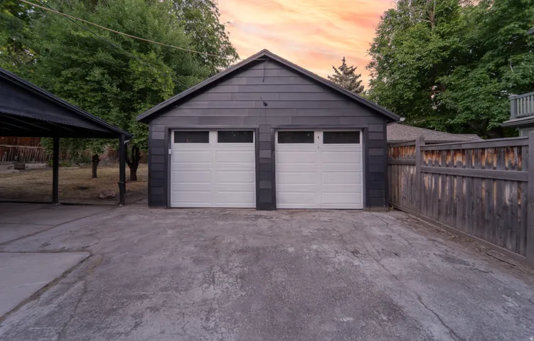 Two-car garage with white paneled doors and upper window inserts, featuring dark gray horizontal siding