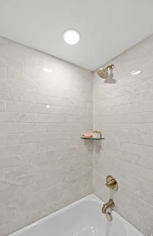 Bathtub and shower combination featuring subway tile surround, recessed lighting, bronze-finish fixtures, and a glass corner shelf