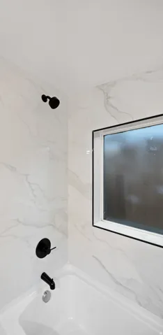 Bathtub with matte black fixtures and a window with black trim