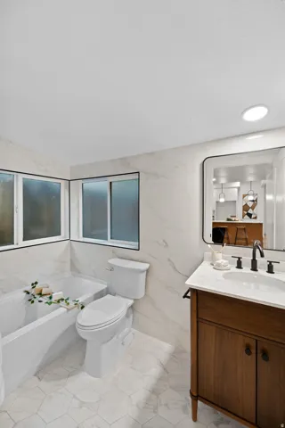 Bathroom featuring a white bathtub, white toilet, and wood-finish vanity with a white countertop