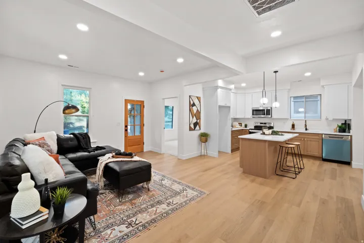 Open-concept living area featuring light wood-finish flooring, recessed lighting, a kitchen island with pendant lighting, white cabinetry, and stainless steel appliances