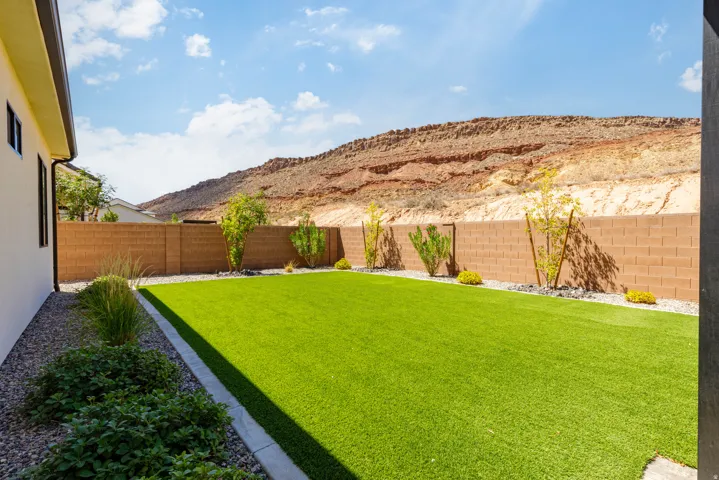 Expansive backyard featuring artificial turf, a block privacy fence, decorative gravel landscaping, and mature shrubbery