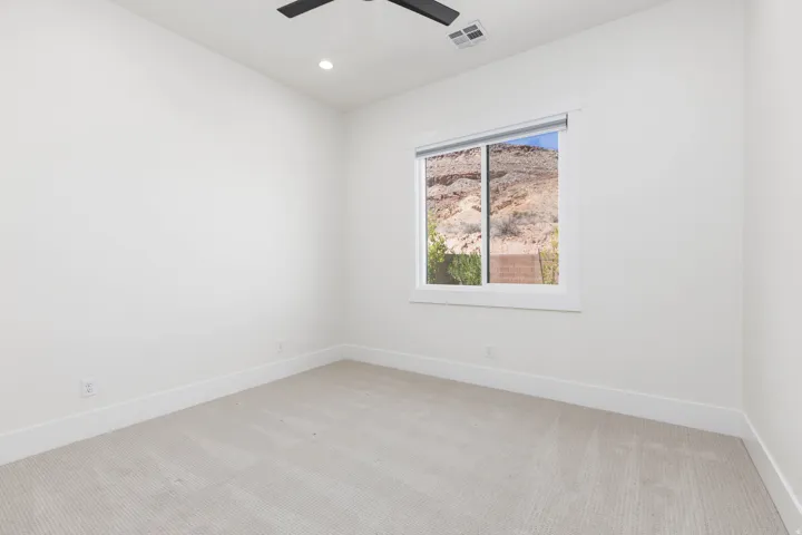 Recessed lighting, ceiling fan, neutral wall tones, window with desert rock formation scenery, and light-toned carpeting