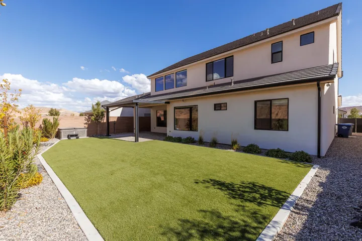 Expansive backyard featuring a manicured artificial turf lawn, gravel borders, and a covered patio structure