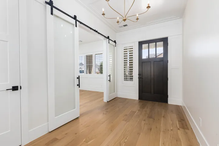 Wood-finish flooring throughout, with a dark-paneled entry door, adjacent window with plantation shutters, and a chandelier light fixture